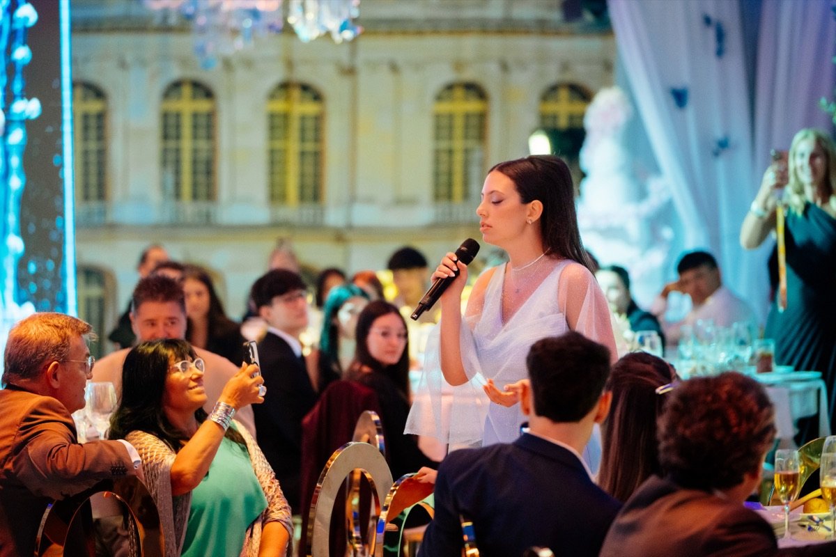 Saint Ninà singing surrounded by statues and chandeliers